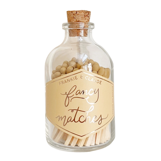 A clear glass bottle with a cork stopper, filled with wooden matches and topped with small round beads. A cream-colored label on the front reads 'FRANKIE & CLAUDE' and 'fancy matches' in elegant script.