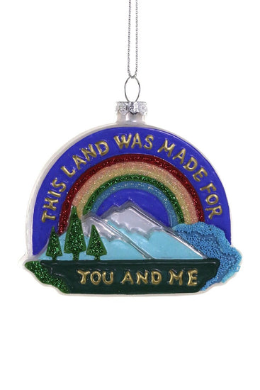 Decorative ornament with rainbow, mountains, trees, and text on a white background